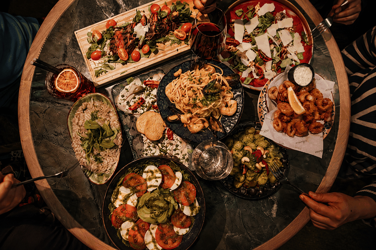 Ronde tafel vol gedeelde schalen: carpaccio, caprese, pasta en calamari