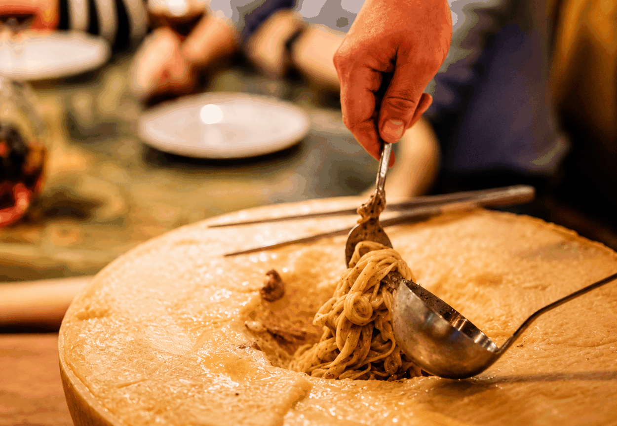 Pasta wordt aan tafel opgeschept uit een heel Parmigiano-kaaswiel